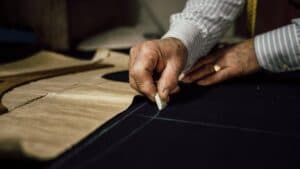 mano di un sarto che con il gesso disegna le misure sulla stoffa da cucire per sartoria Milano