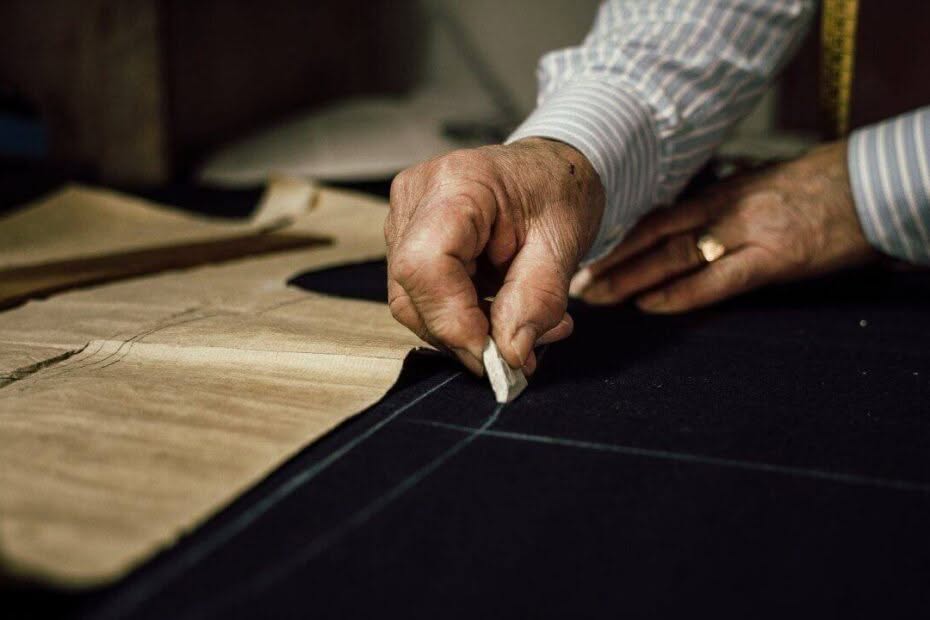 mano di un sarto che con il gesso disegna le misure sulla stoffa da cucire per sartoria Milano